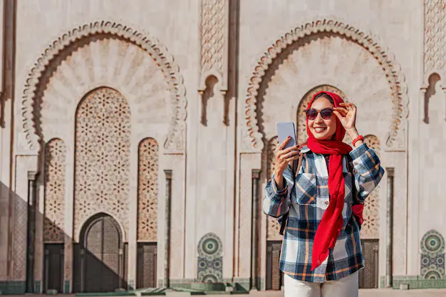 smiling tourist wearing red hijab sunglasses using smartphone front hassan ii mosque casablanca morocco